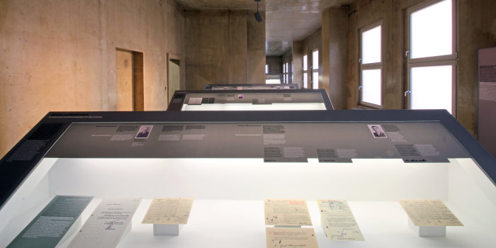 Farbfotografie, vorne großes Pult mit Glasabdeckung, darunter mehrere alte Dokumente, im Hintergrund weitere Pulte