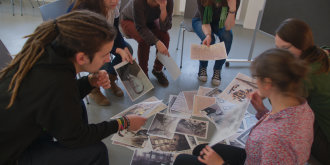 Gruppe von fünf Personen im Stuhlkreis mit mehreren Fotos auf dem Boden in der Mitte