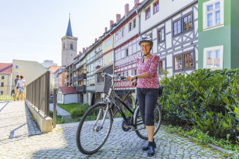 Frau auf dem Fahrrad, dahinter mittelalterliche Häuser.