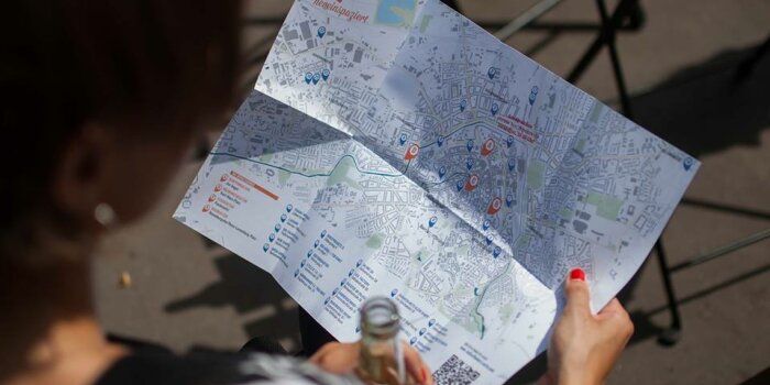 eine Frau hält eine Flasche und einen Stadtplan von Erfurt in der Hand, in dem einzelne Orte hervorgehoben sind