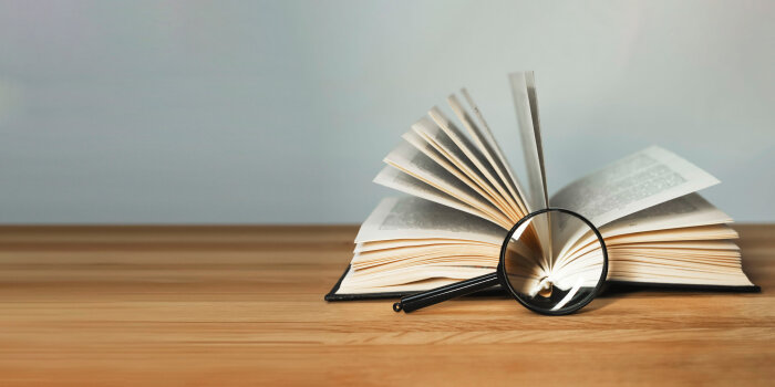 Aufgeschlagenes Buch auf Tisch mit Lupe