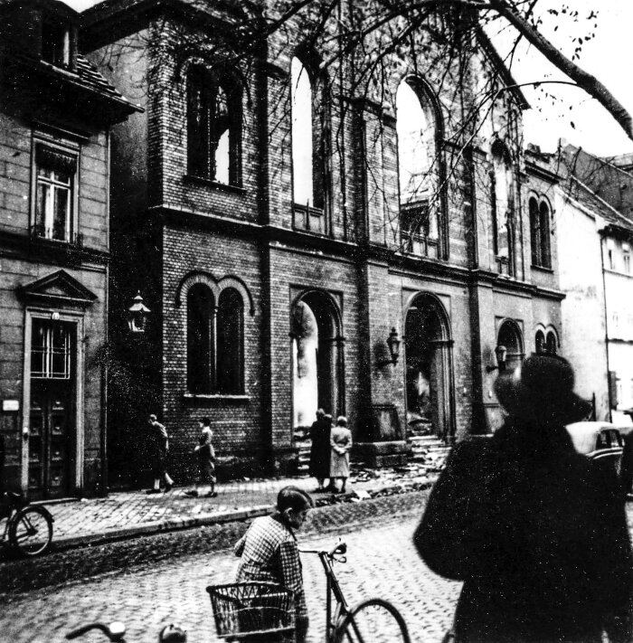 Zerstörte Große Synagoge mit Passanten historische Aufnahme einer Gebäudefassade, hinter der Zerstörung zu erkennen ist