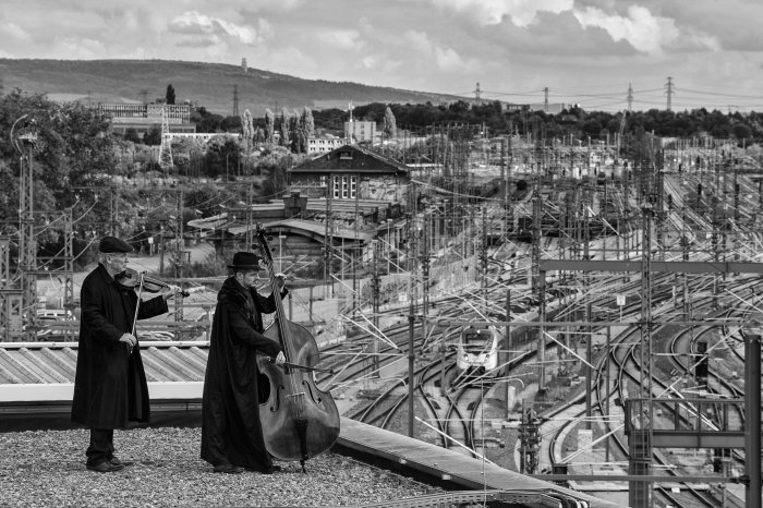 Zwei Männer, in schwarz gekleidet spielen Streichinstrumente. Im Hintergrund der Erfurter Bahnhof.