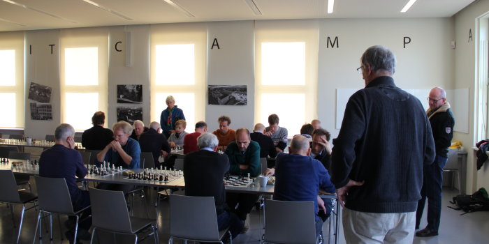 Mehrere Menschen sitzen an Tischen. Sie spielen Schach.