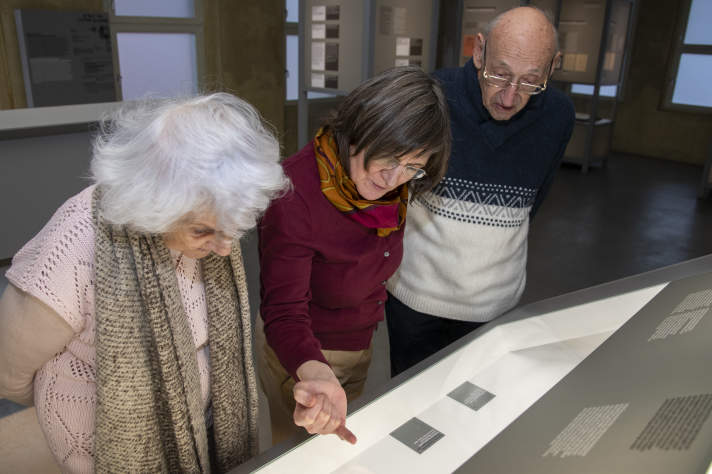 Eine Frau steht in einer Ausstellung und zeigt auf ein Pult.