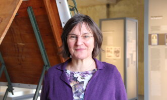 Eine Frau mit lila Jacke in einer Ausstellung.