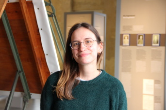 Lisa Caspari, Projektmitarbeiterin Eine Frau mit Brille und grünem Oberteil in einer Ausstellung.