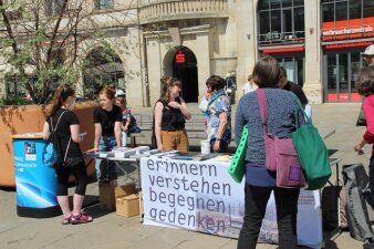 fünf Personen stehen um einen Tisch mit der Aufschrift erinnern verstehen begegnen gedenken 