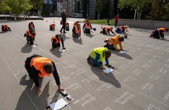 mehrere Personen in Warnweste die kniend Namen auf einen Platz schreiben 