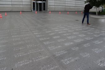 mehrere mit Kreide geschriebene Namen auf einen Platz und eine Person die sie fotografiert 