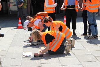 drei Jugendliche mit Warneste knien in einer Reihe und schreiben mit Kreide  