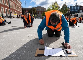 mehrere Personen in Warnweste die kniend Namen auf einen Platz schreiben