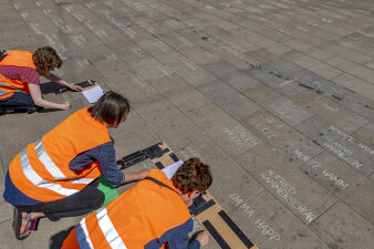 Drei Personen knien auf dem Boden und schreiben Namen auf die Straße