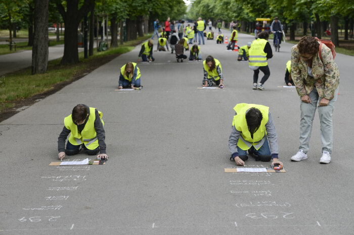 viele Menschen mit gelber Warnweste kniend und schreibend auf einer Straße 