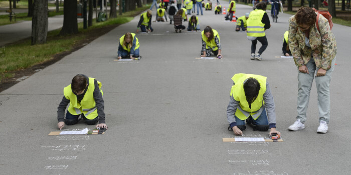 viele Menschen mit gelber Warnweste kniend und schreibend auf einer Straße 