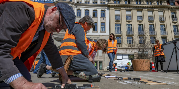 drei Personen mit Warnweste die Namen mit Kreide auf den Bahnhofsvorplatz schreiben 