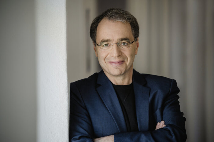 David Safier Lächelnder Mann mit Brille, der an deiner Wand lehnt