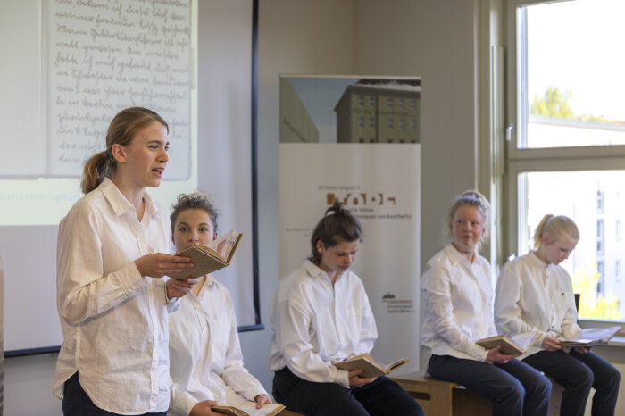 Fünf Jugendliche in weißen Hemden, die aus einem Buch vorlesen 