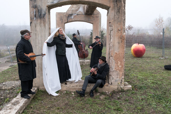 Gedenkkonzert von The String Company Erfurt an der zerstörten Viehauktionshalle in Weimar Vier Männer mit Instrumenten, in der Mitte eine Frau mit eingehüllt in ein weißes Tuch