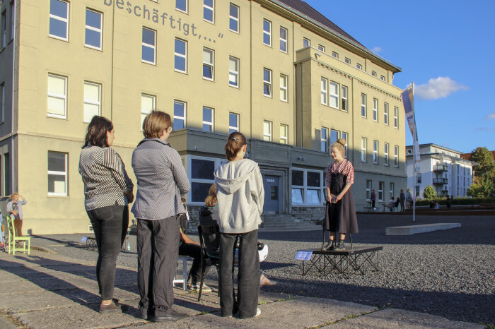 Lesung mit dem Theater „Die Schotte“ eine Person steht auf einer kleinen Bühne, weitere Personen hören zu
