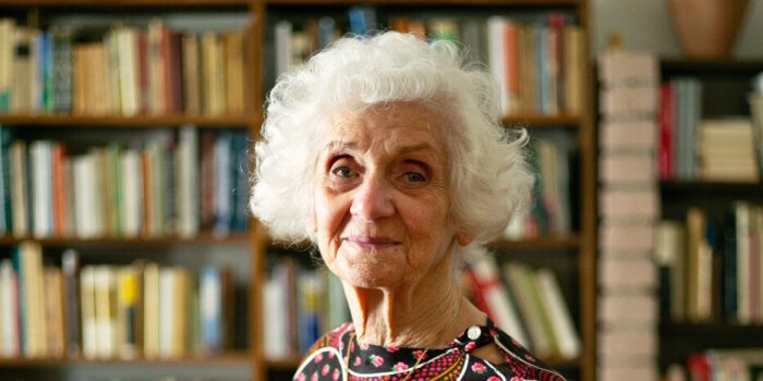 Ältere Frau mit farbigem Kleid vor einem Bücherregal