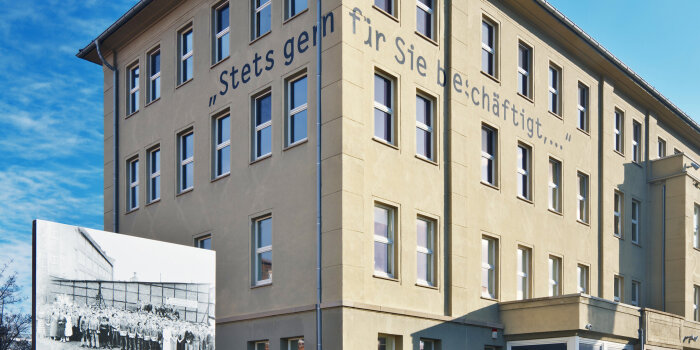 vierstöckiges Gebäude mit Schriftzug "Stets gern für Sie beschäftigt, ..."