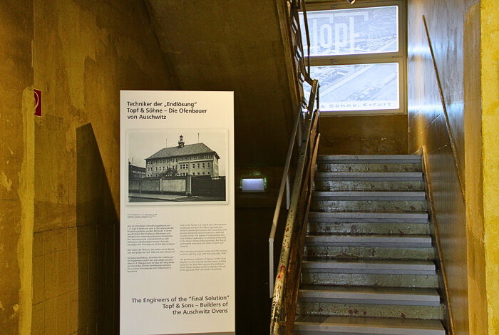 Hinterleuchtete Stele neben einem dunklen Treppenaufgang