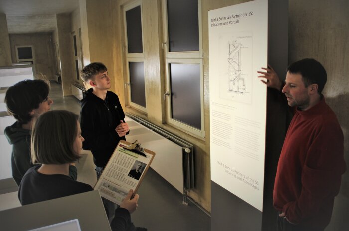 Personen in einer Ausstellung neben einer hinterleuchteten Stele