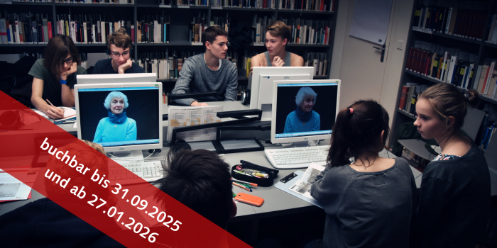 Mehere Personen in einem Raum mit vielen Büchern und vier Computern 