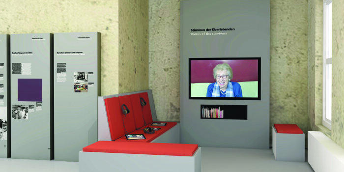 Ausstellungsraum mit Schautafeln, Sitzmöglichkeit und einer Videopräsentation auf einem Bildschirm