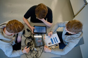 Drei Personen an einem Tisch die in iPads schauen  
