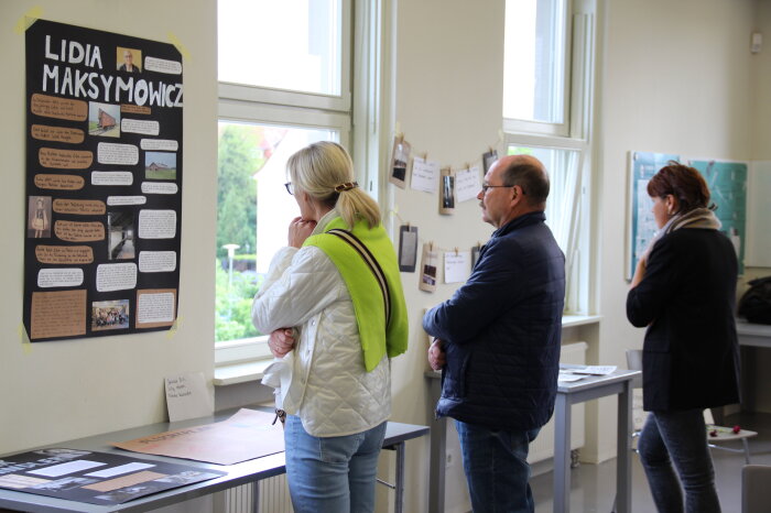 Drei Personen schauen sich Plakate für Schülern zu ihrer Gedenkstättenfahrt an.