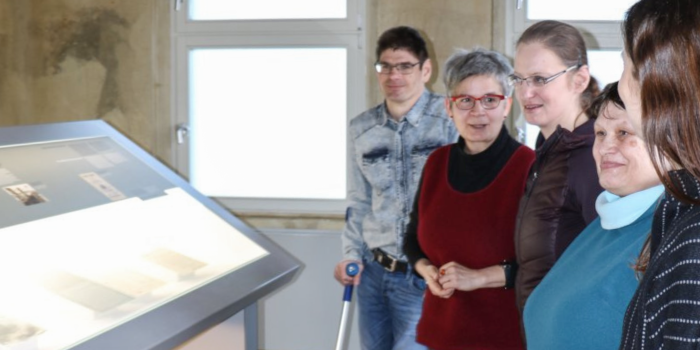 Gruppe steht mit Guide vor Ausstellungspult