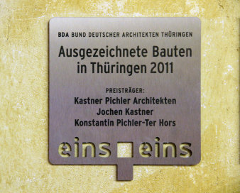 Farbfoto, gelbe Wand, auf der eine Plakette aufgeschraubt ist mit Schriftzug BDA Bund deutscher Architekten Thüringen Ausgezeichnete Bauten in Thüringen 2011 Preisträger Kastner Pichler Architekten Jochen Kastner Konstantin Picher-Ter Hors