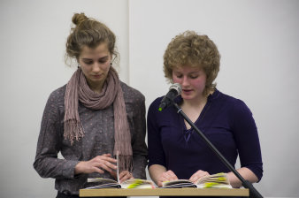 Zwei junge Frauen stehen am Mikrofon und lesen aus einem Buch