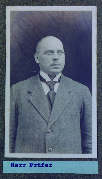 Schwarz-Weiß-Fotografie eines jungen Mannes im Anzug mit Krawatte, trägt Brille, unter der Fotografie der Name Kurt Prüfer in Druckschrift