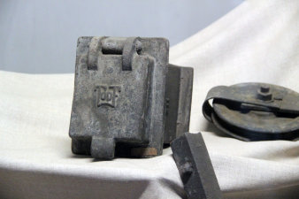 Farbfotografie, alte Eisenteile auf weißem Tuch gelegt, eine Klappe darunter mit Topf-Logo drauf