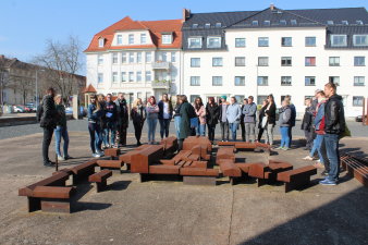 Junge Menschen stehen bei dem Modell des Firmengeländes. Eine Häuserfassade erstreckt sich im Hintergrund. 