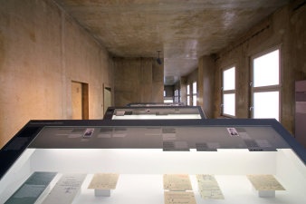 Farbfotografie, vorne großes Pult mit Glasabdeckung, darunter mehrere alte Dokumente, im Hintergrund weitere Pulte