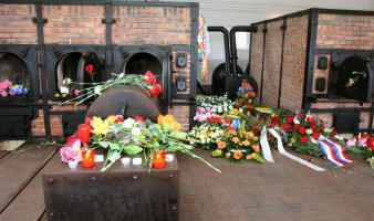 Ofen aus Backstein und Stahlgerüst, vor und neben dem Ofen Blumen, Kerzen und Kränze