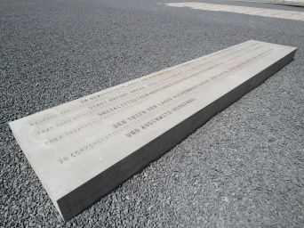 Länglicher Betonstein mit eingravierter Schrift in der Bildmitte