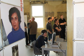 Farbfoto, mehrere Personen stehend, eine Person sitzt mit Kopfhörern an einem Monitor