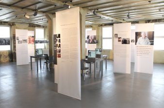 Farbfotografie, großer heller Raum mit mehreren weißen bedruckten Bannern, Tische mit Monitoren und Kopfhörern