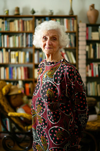 Eine ältere Frau steht vor einem Bücherregal.