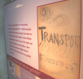 Tafel in einer Ausstellung mit aufgedrucktem Bild, auf dem groß "Transport" steht. Daneben Text.