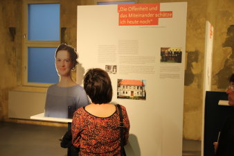 Farbfoto, Frau steht vor Tafel mit Text und Bildern