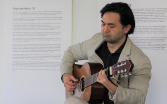 Ein Gitarrist spielt vor Ausdrucken von Schwarz-Weiß-Fotos mit Texten zur Ausstellungseröffnung.