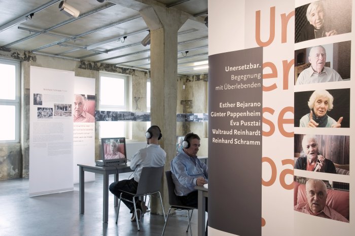 Blick in die Ausstellung "Un-er-setz-bar. Begegnung mit Überlebenden" Blick in den Raum mit Tafeln. Besucher benutzen Multimediageräte