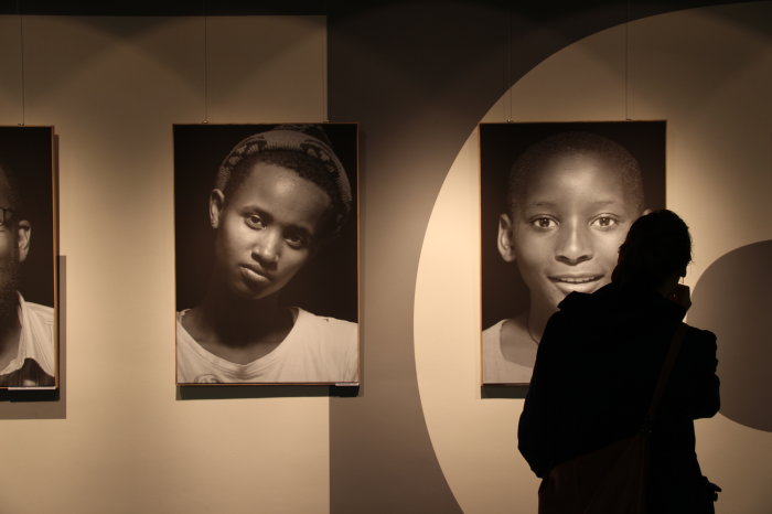 Rechts im Bild steht eine Person vor zwei übergroßen Schwarz-Weiß-Fotografien, die jeweils ein Einzelporträt von einem Kind als Schulterstück zeigen.