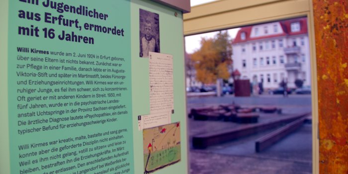 Eine Ausstellungstafel mit einem Schwarz-Weiß-Foto und einer Kinderzeichnung, im Hintergrund ist ein Fenster.